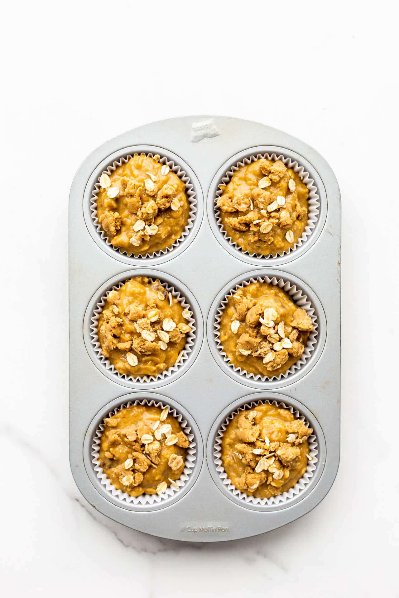Banana muffins topped with oats ready to be baked in a muffin pan.
