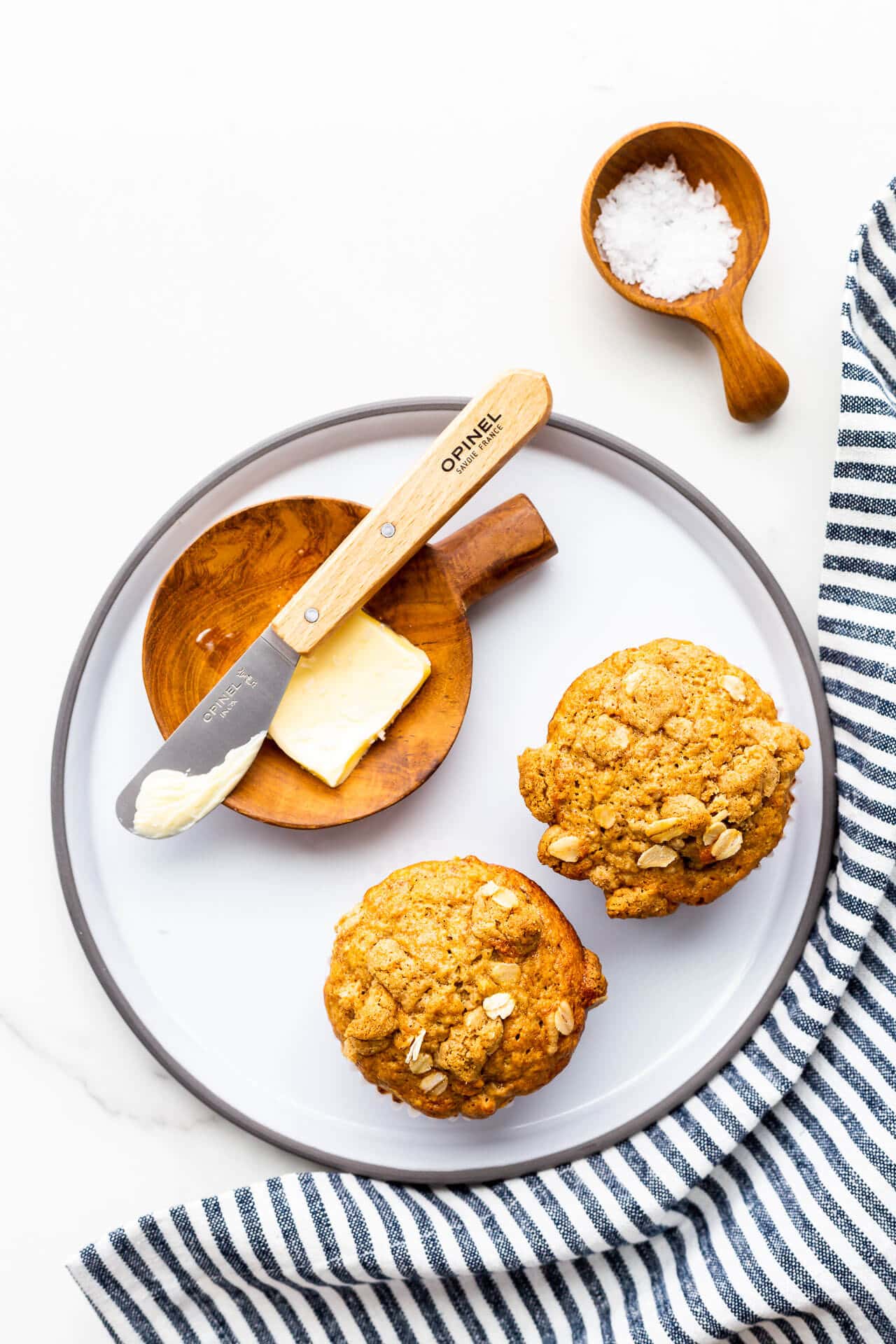 Banana muffins on a grey plate with butter and a butter knife, and sea salt.