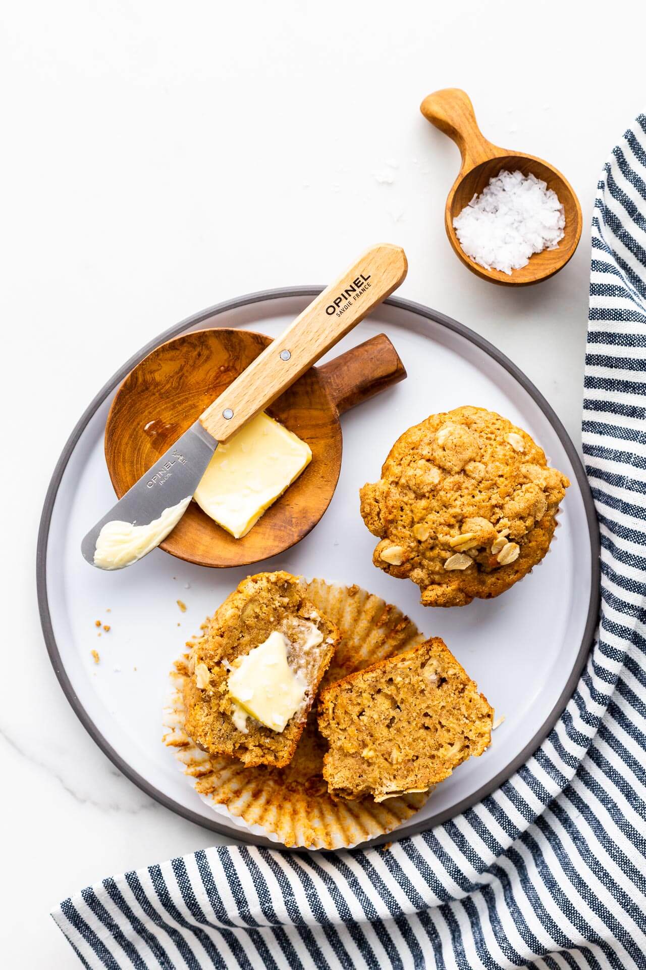 Banana muffins on a grey plate with butter and a butter knife, and sea salt.