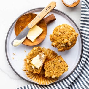 A grey-rimmed ceramic plate with two banana muffins, one split open and buttered.