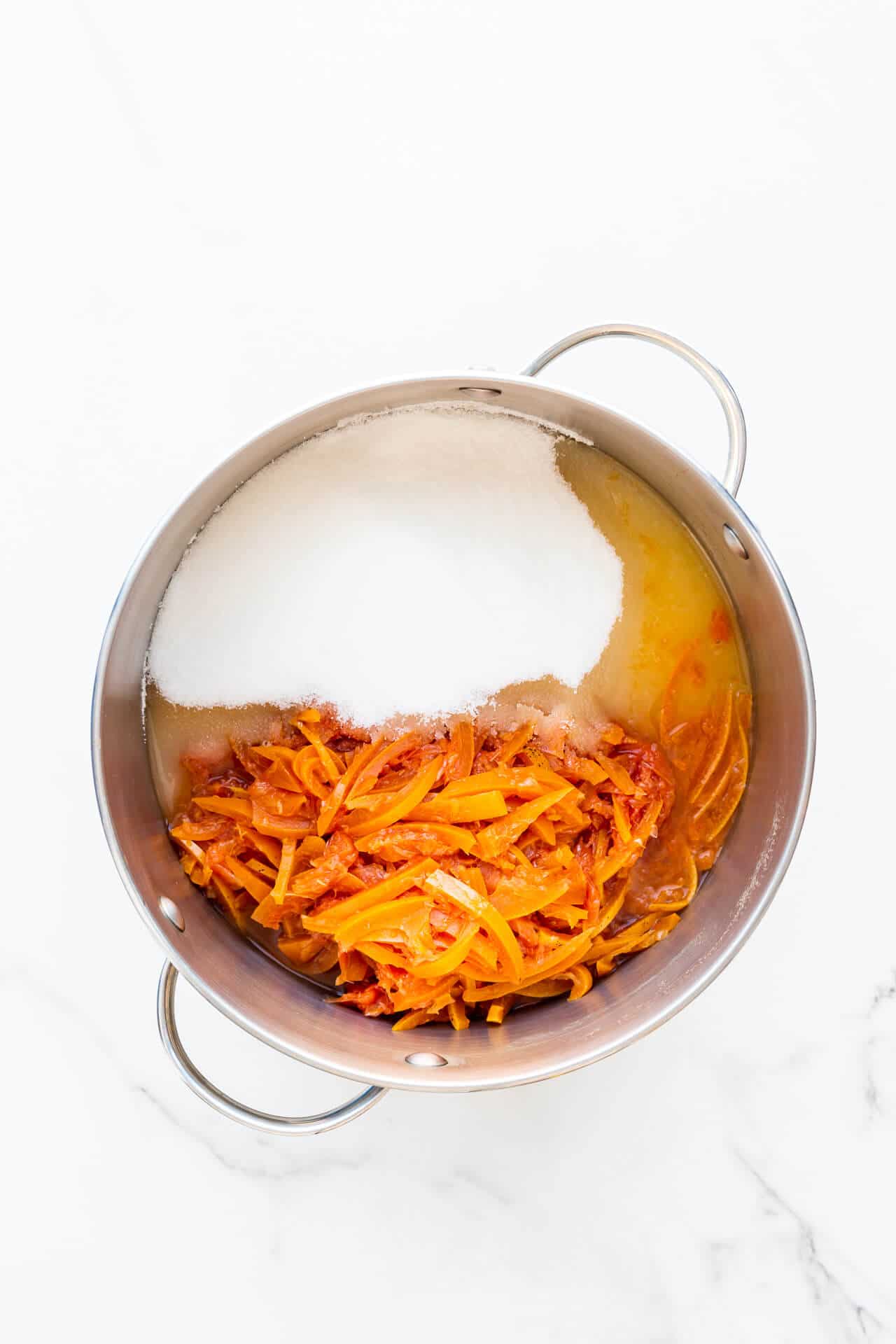 A stainless steel pot with sliced citrus fruit, sugar, and lemon juice, ready to make marmalade.