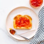 Pink grapefruit marmalade on toast on a plate with a striped linen.