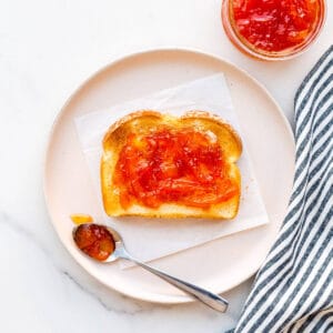Pink grapefruit marmalade on toast on a plate with a striped linen.