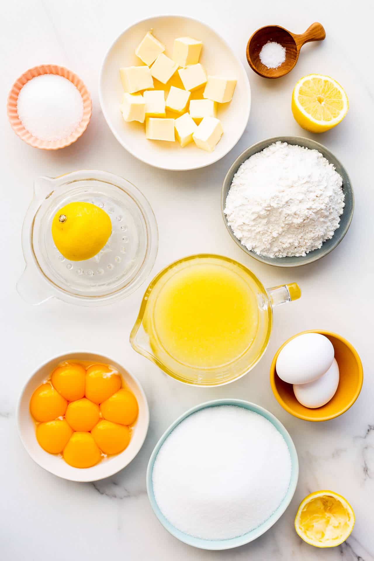 Ingredients to make lemon bars from scratch measured out, including butter, sugar, salt, lemons, lemon juice, flour, eggs and egg yolks.