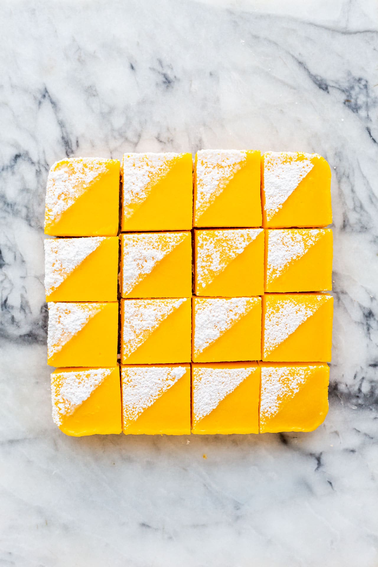 Lemon bars cut into squares and decorated with icing sugar on a marble surface.