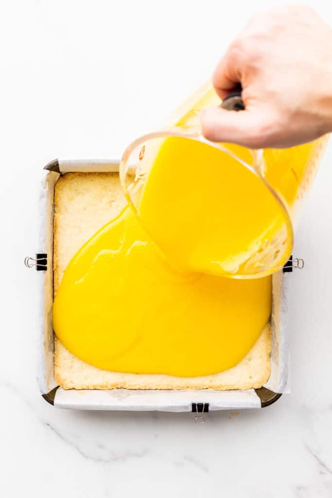 Pouring lemon curd over a shortbread crust to make lemon bars.