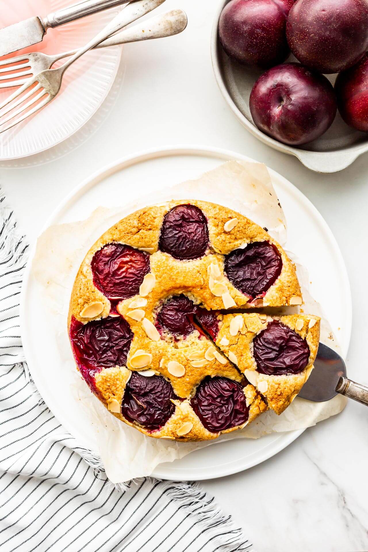 Cake with plums being sliced and served with a cake lifter.