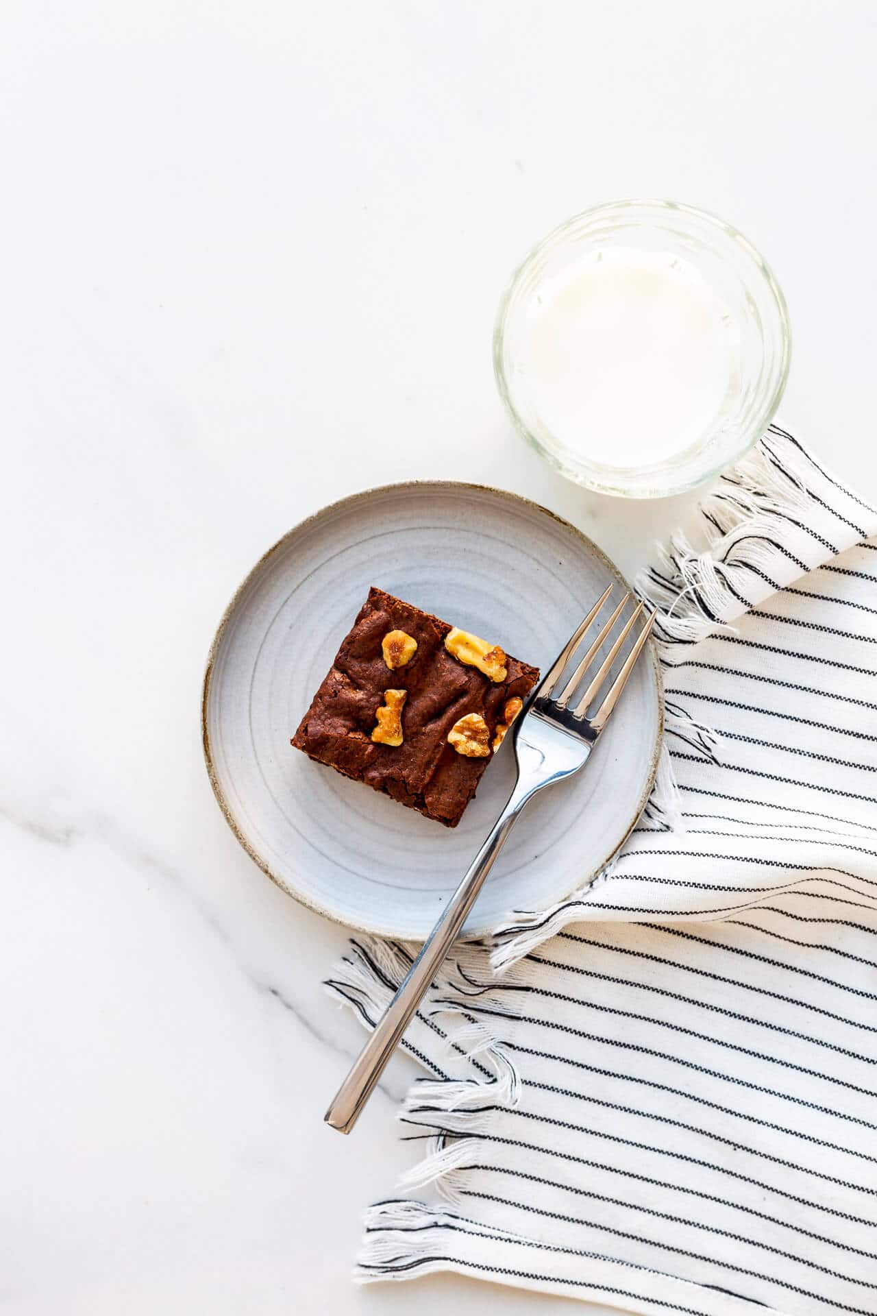 A brownie with walnuts on a ceramic plate with a fork.