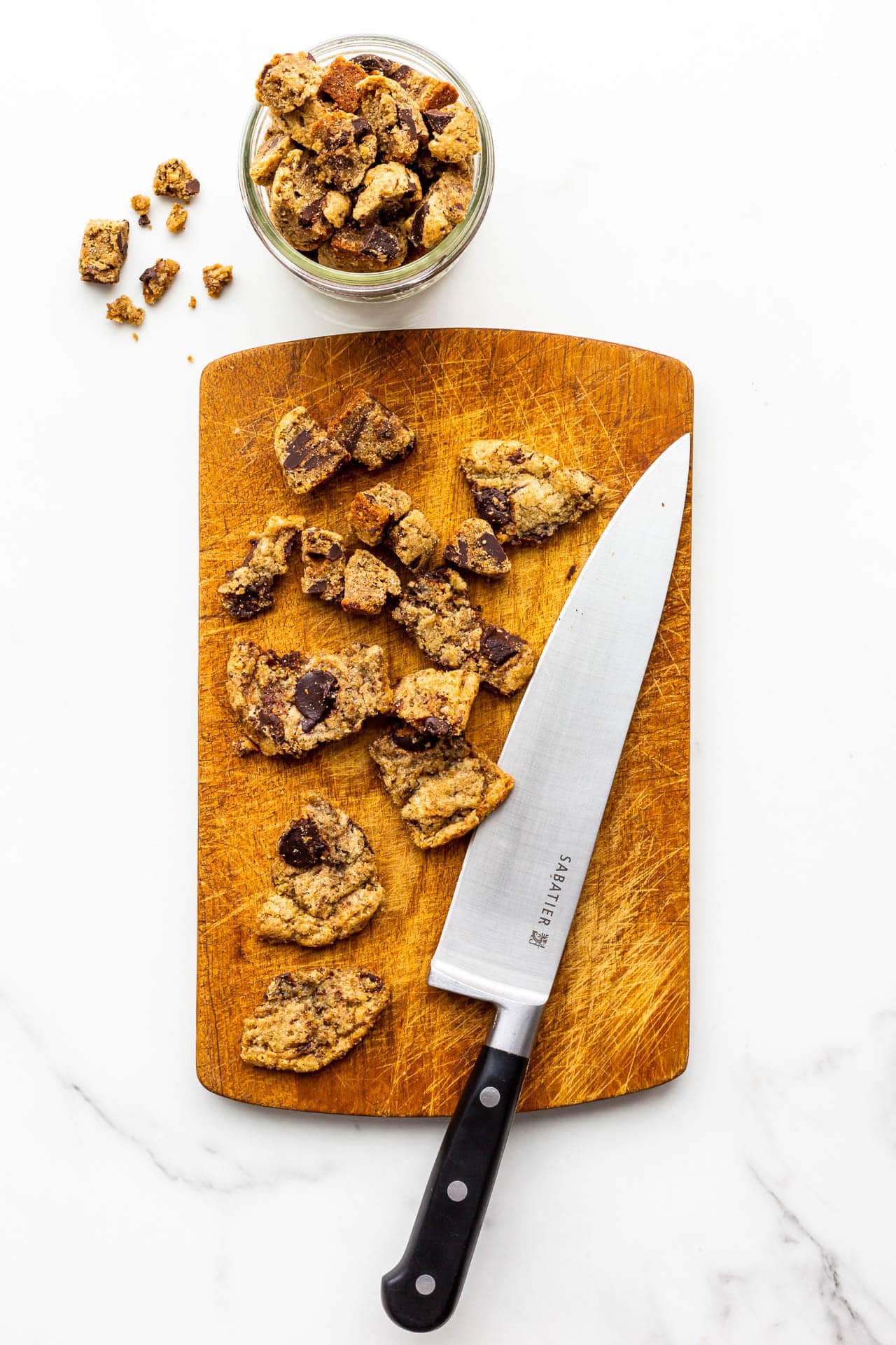 Chopping homemade chocolate chip cookies on a wood cutting board with a chef's knife to use in a recipe for cookie ice cream.