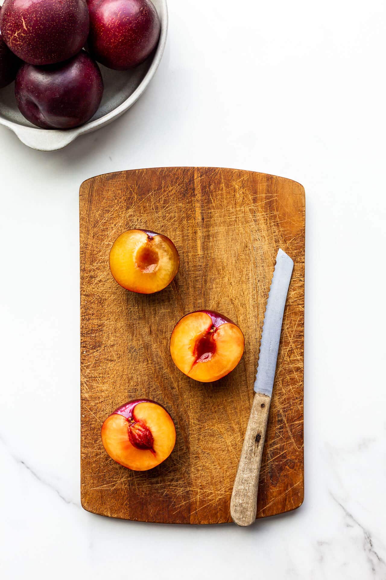 Slicing fresh plums in half to remove pit so you can garnish a cake with the fresh fruit.