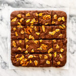 Brownies with walnuts cut into squares on a marble surface.