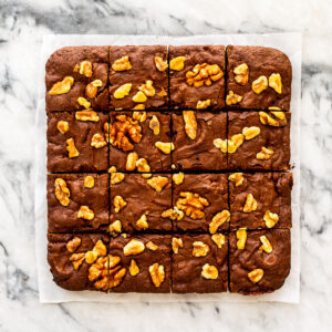 Brownies with walnuts cut into squares on a marble surface.