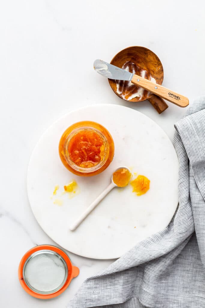 An open jar of orange marmalade on a marble surface.