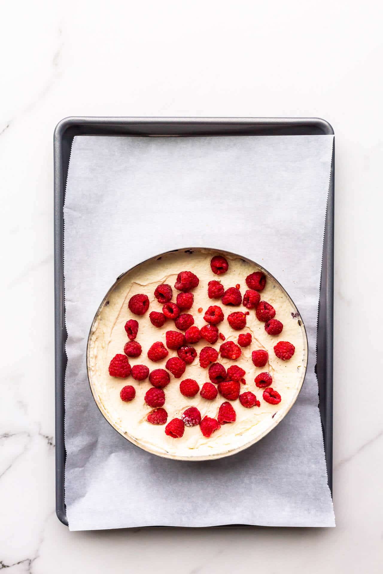 Filling a framboisier cake in a cake ring with mousseline cream and fresh raspberries.