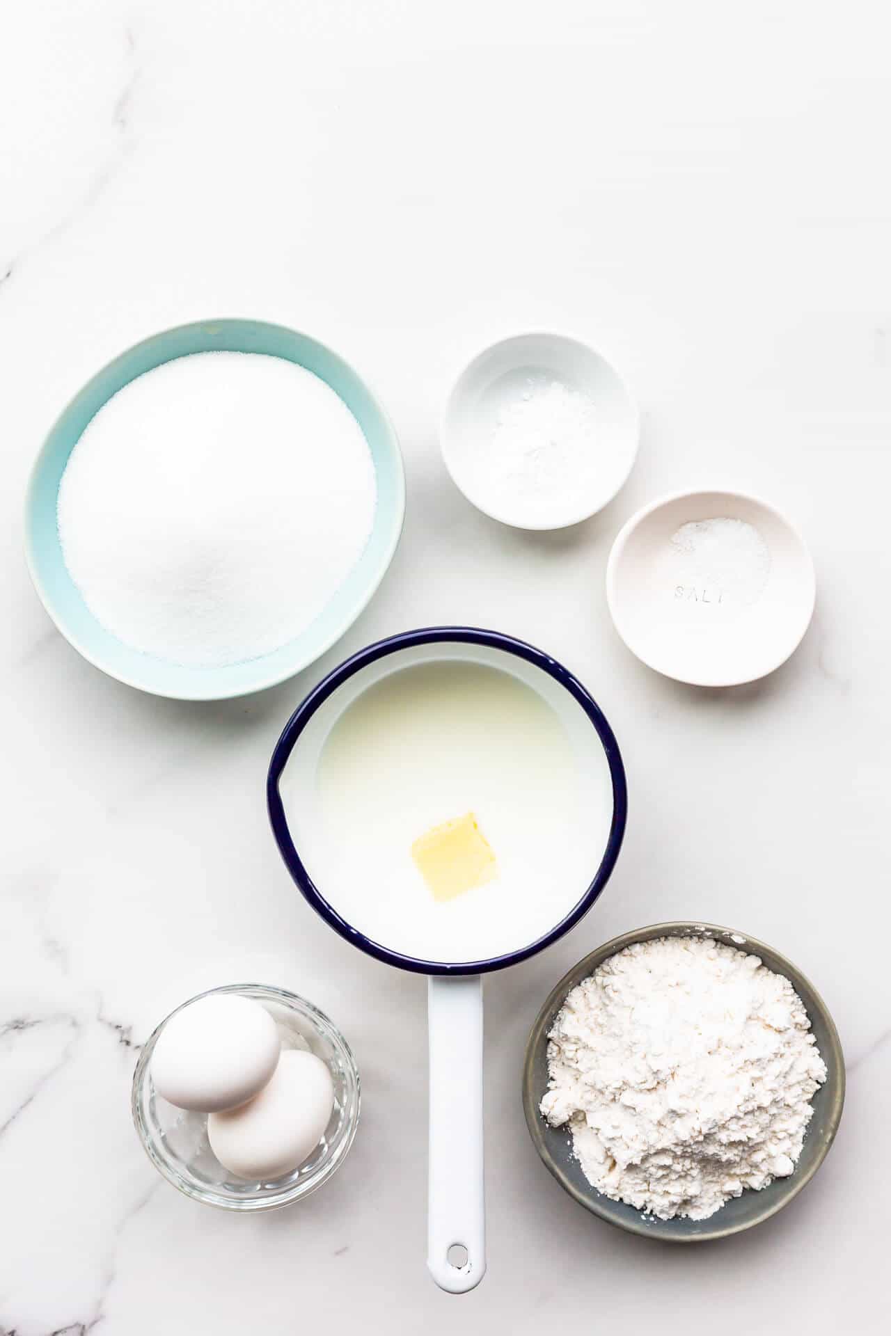 Ingredients to make an easy sponge cake called the hot milk sponge cake, measured out, including flour, eggs, sugar, baking powder, salt, and milk with butter in a saucepan.