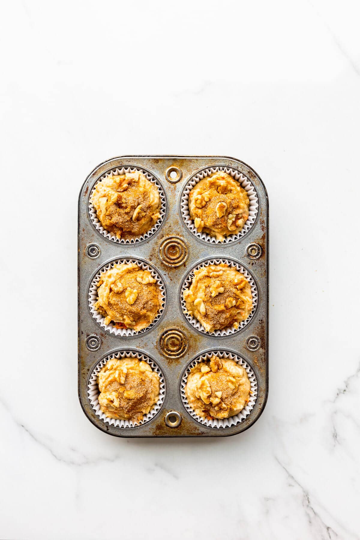 Carrot muffins topped with cinnamon sugar before baking in muffin pan with paper liners.