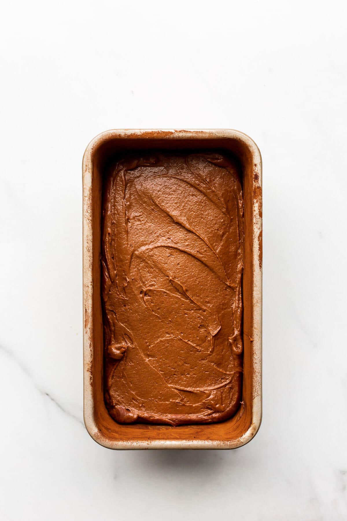 Chocolate cake batter spread evenly in a loaf cake pan, ready to be baked.
