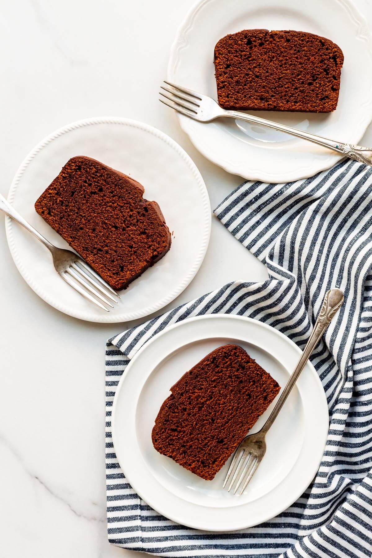 Slices of chocolate loaf cake on white plates and striped linen, ready to be served,