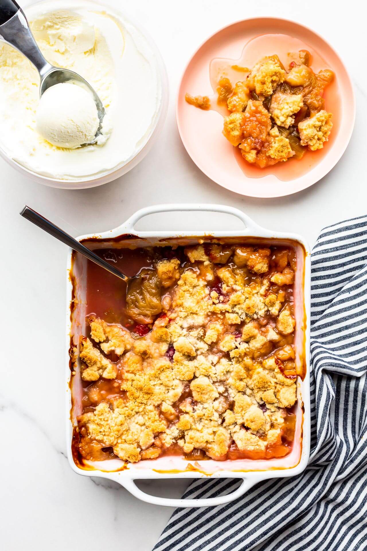 Warm rhubarb crisp in an 8x8-inch white ceramic baking dish served on plates with vanilla ice cream.