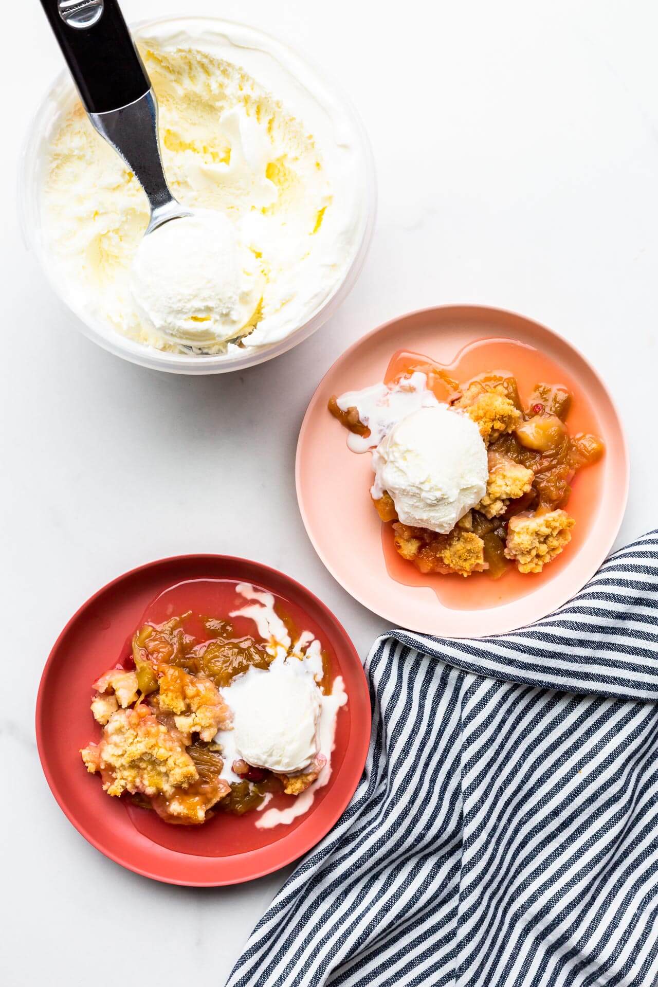 Rhubarb crumble served warm on pink plates with scoops of vanilla ice cream.