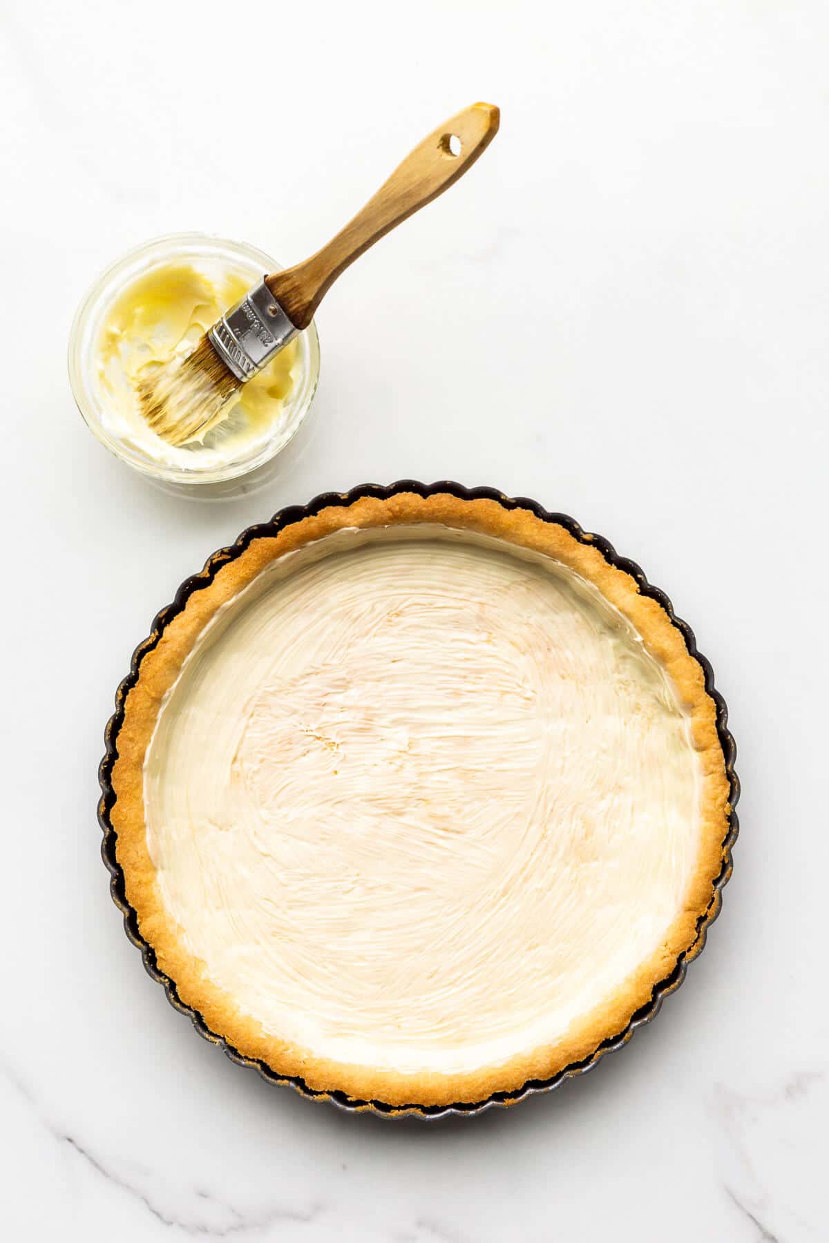 Brushing a baked tart shell with melted white chocolate to seal the pastry crust before filling.