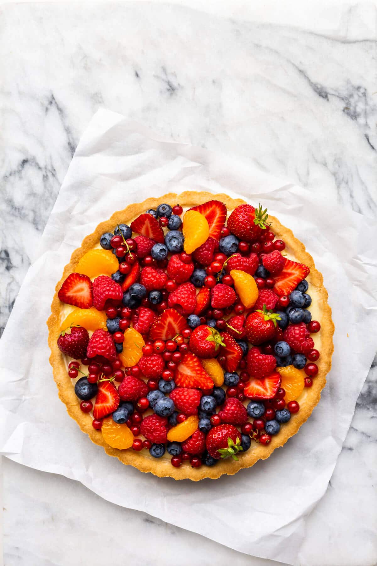 Fruit tart with vanilla pastry cream on parchment paper on marble.