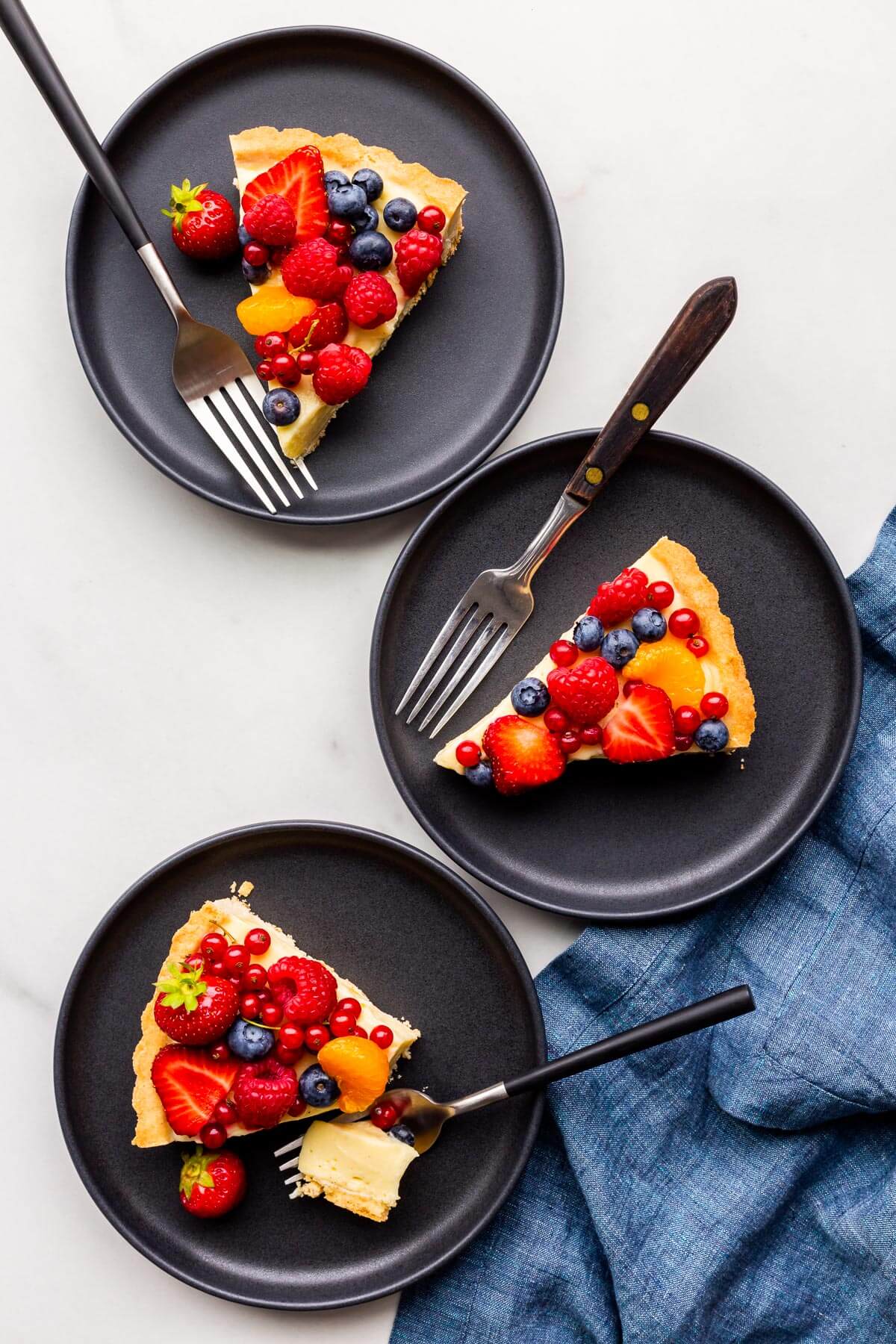 Slices of fruit tart served on black dessert plates.