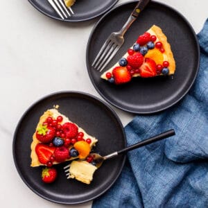 Slices of fruit tart served on black dessert plates.