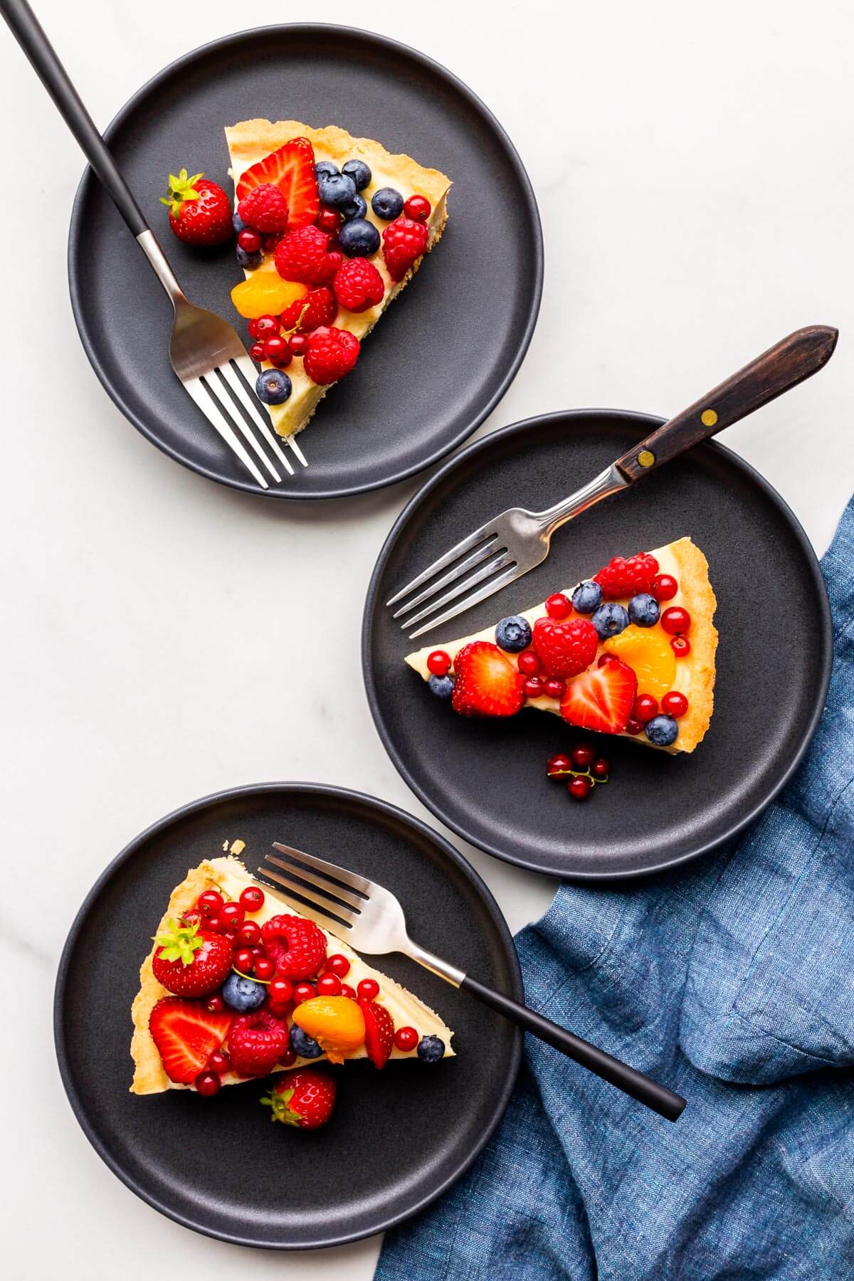 Slices of fruit tart served on black dessert plates.