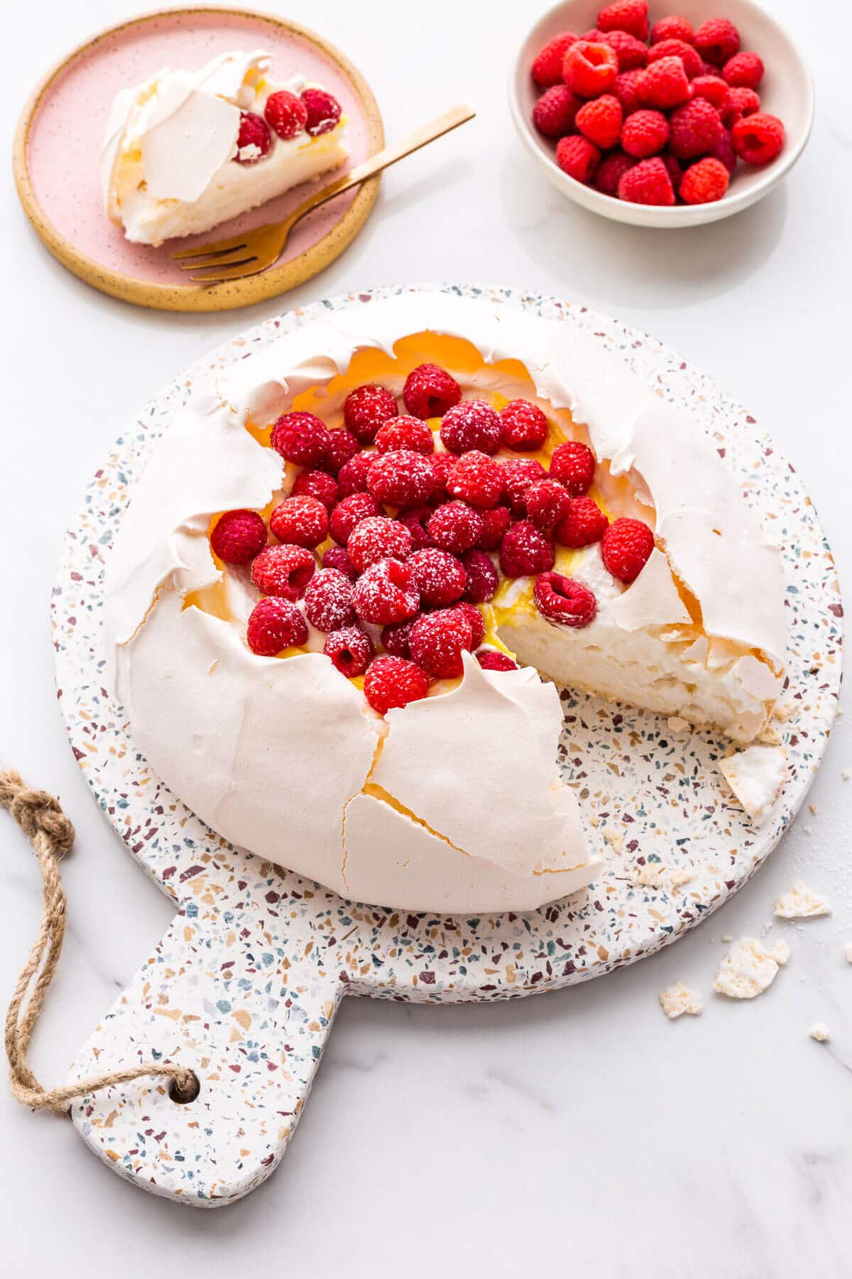 Pavlova cake filled with whipped cream, lemon curd, and raspberries being served.