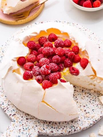 Pavlova cake filled with whipped cream, lemon curd, and raspberries being served.