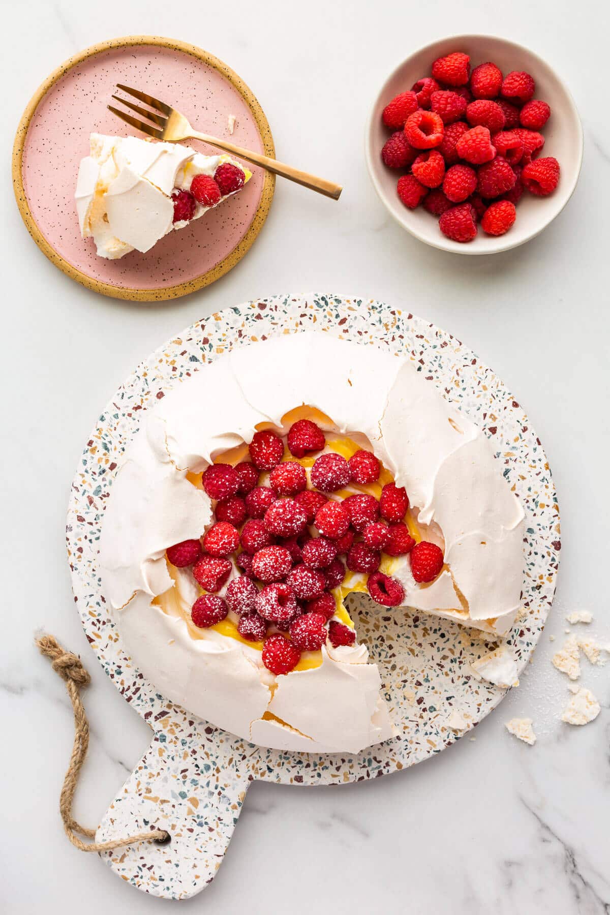 Pavlova cake filled with whipped cream, lemon curd, and raspberries being served.