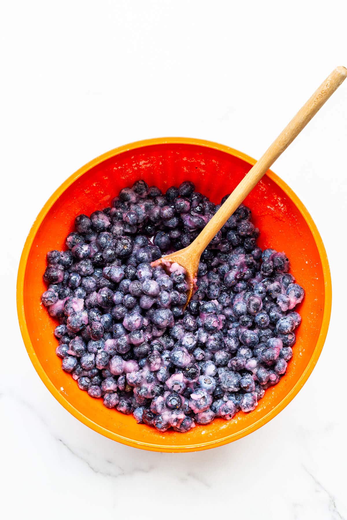 A big bowl of macerated blueberries with sugar and lemon juice ready to be boiled in a big pot to make homemade blueberry jam.