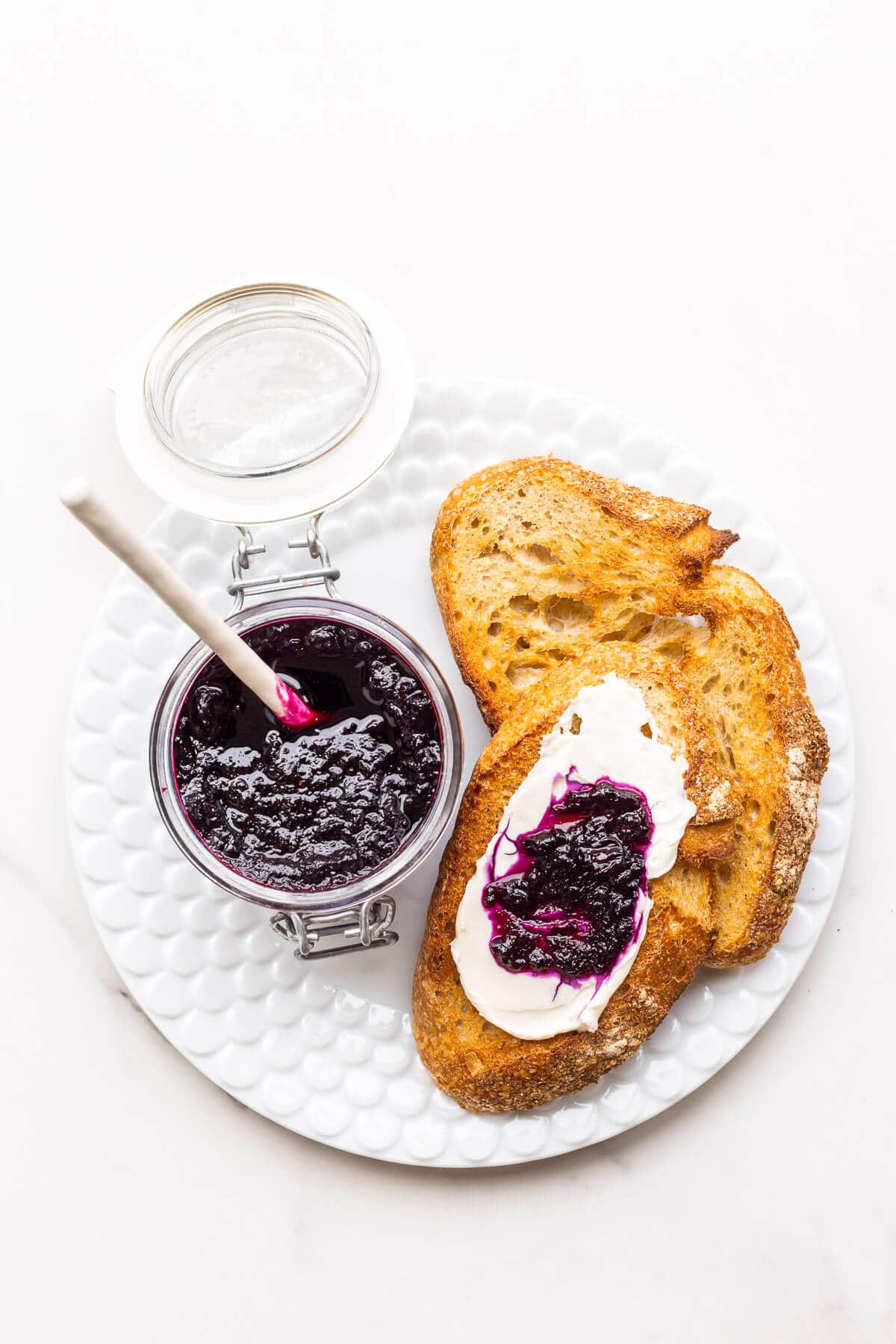 A jar of homemade blueberry jam served with cream cheese and toasted sourdough on a plate.