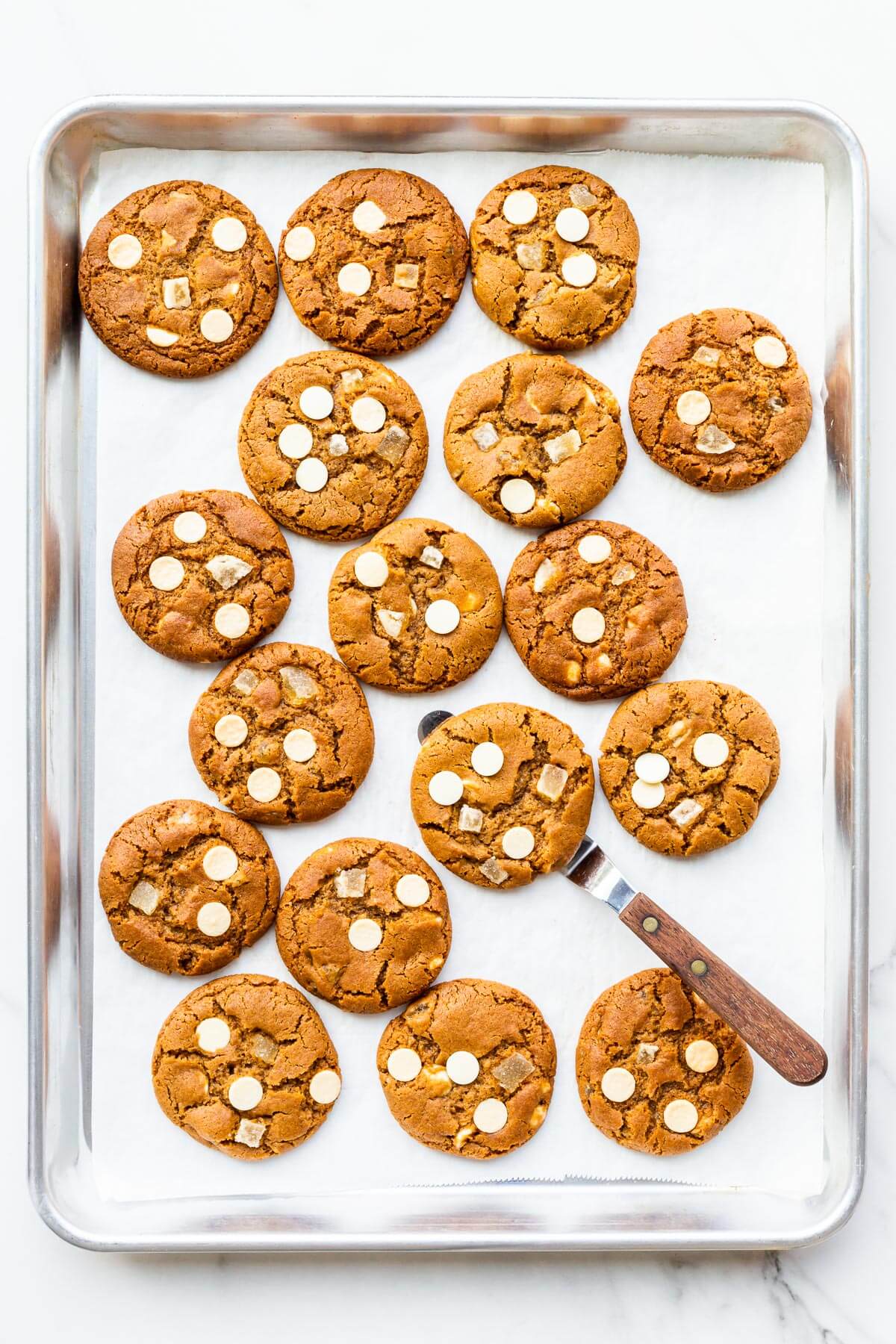 Freshly baked ginger white chocolate cookies cooling slightly on a sheet pan to firm them up before transferring to a cooling rack.