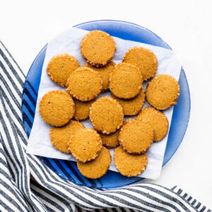 A plate of round gingerbread cookies with crunchy turbinado sugar edges served with a cup of coffee.