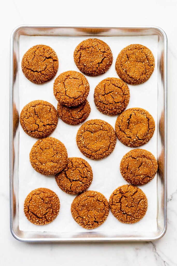 Freshly baked molasses cookies coated in turbinado sugar on a parchment-lined sheet pan.