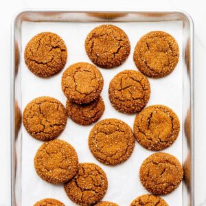 Freshly baked molasses cookies coated in turbinado sugar on a parchment-lined sheet pan.