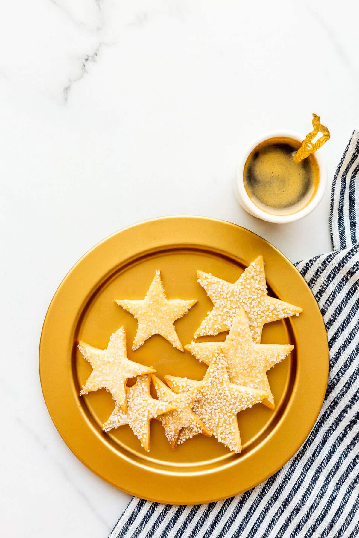 A gold plate of sugar cookie stars with a cup of coffee.