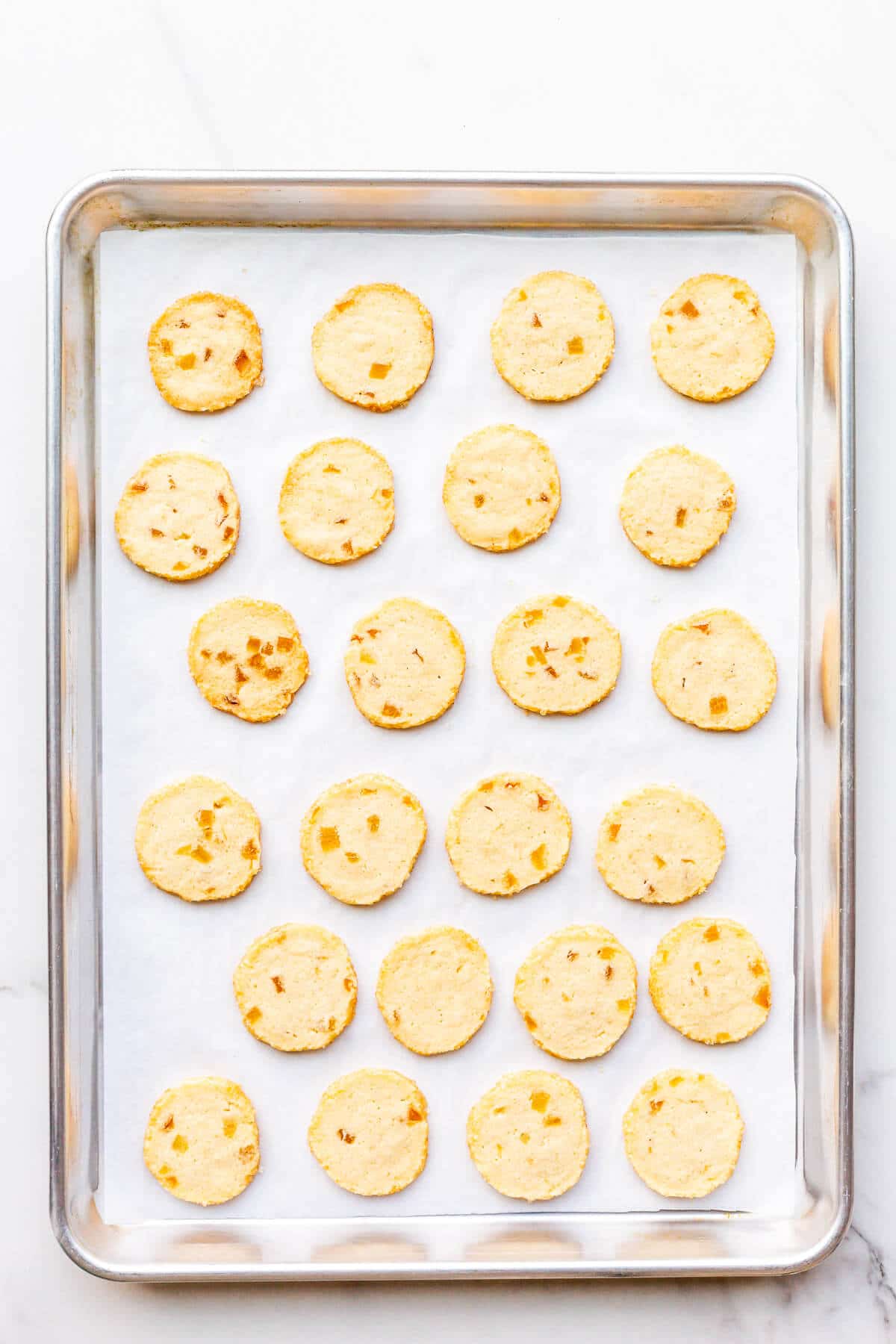 Freshly baked slice-and-bake cookies with crystallized ginger on a parchment-lined sheet pan.