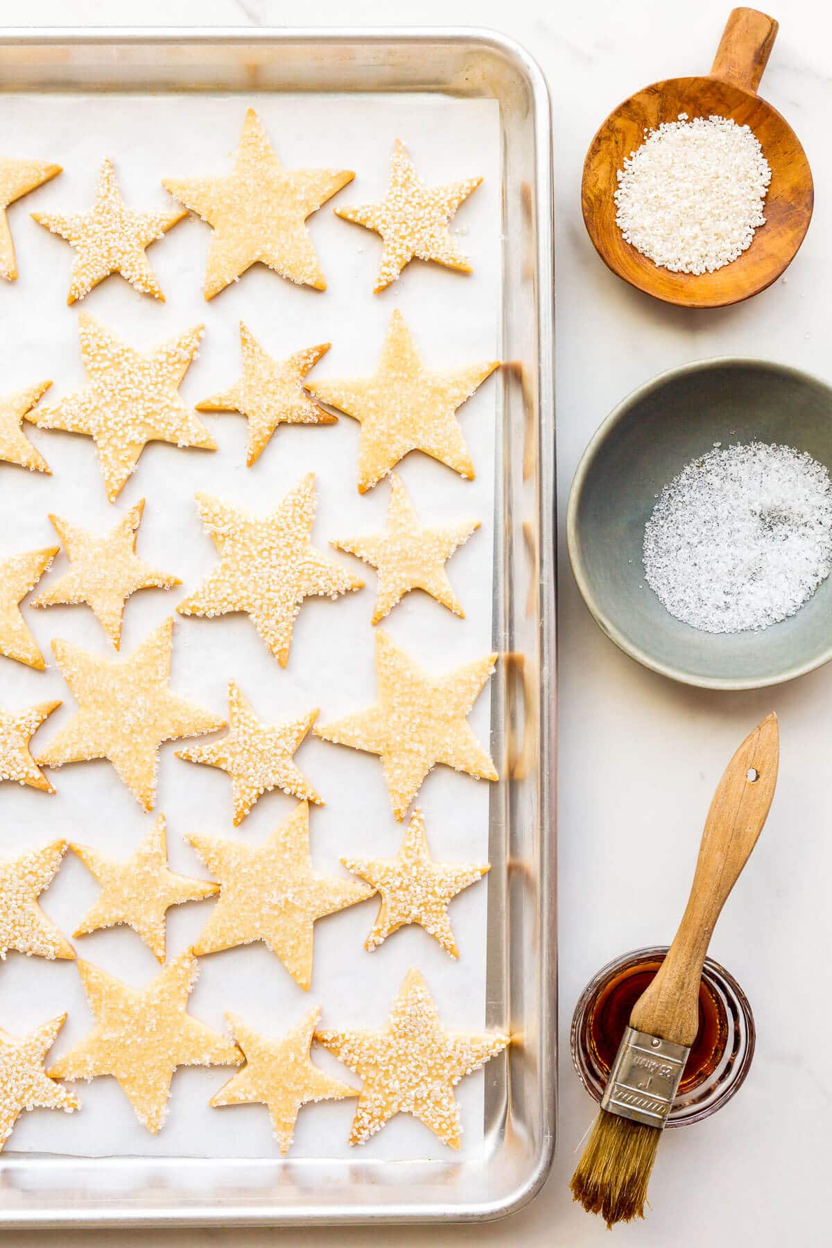 Brushing freshly baked sugar cookies with maple syrup and coating in sparkly sanding sugar.