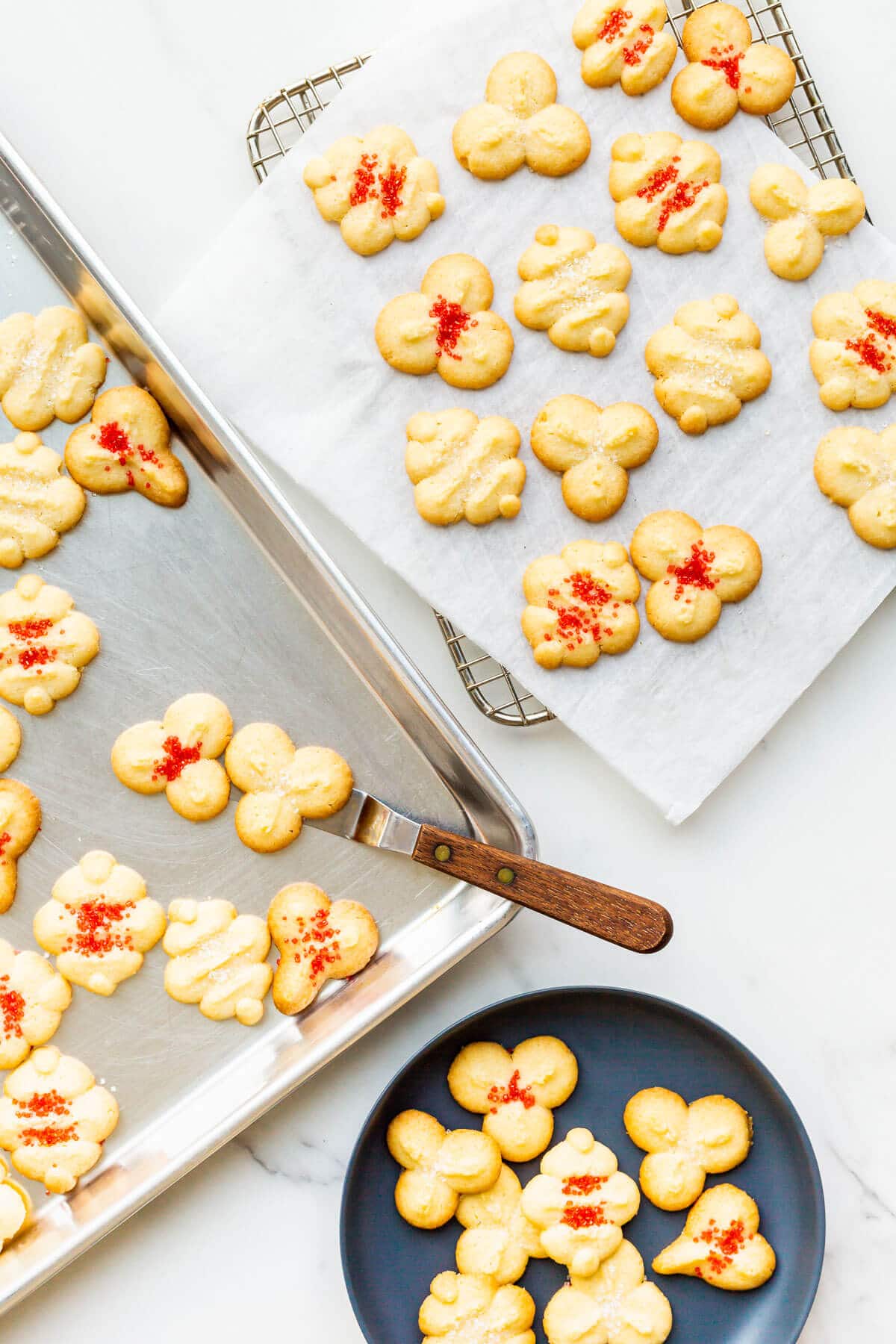 Trasnferring spritz cookies to a cooling rack and then serving on a black plate.