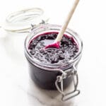 A jar of homemade blueberry jam with a spoon.