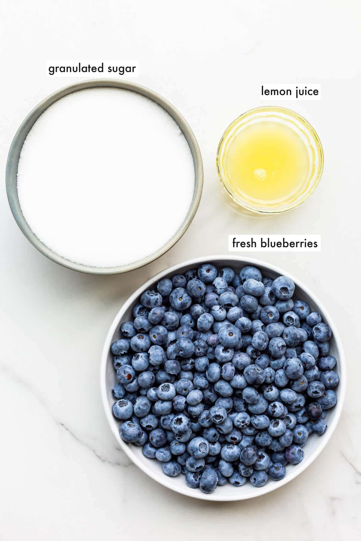 The three ingredients needed to make homemade blueberry jam, including fresh blueberries, granulated sugar, and lemon juice.