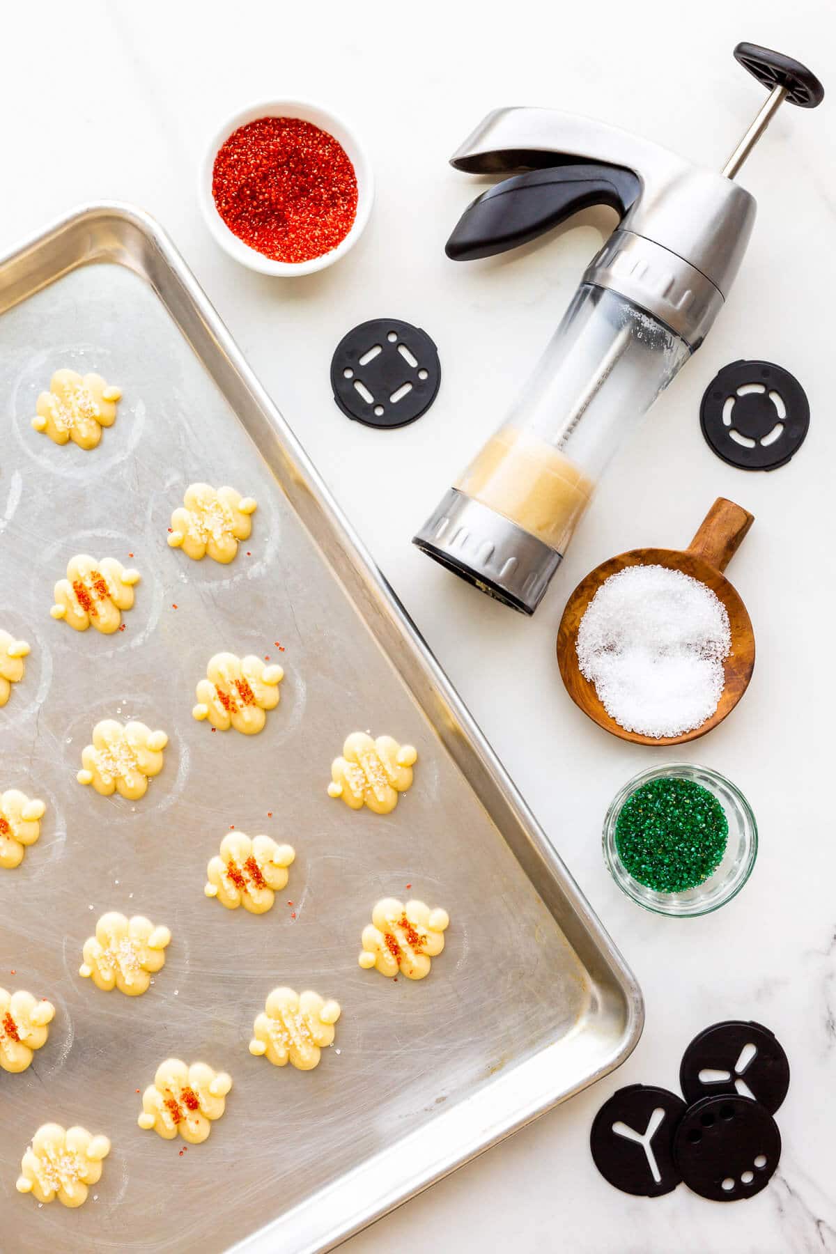 Using a cookie press to press out spritz cookies on an ungreased cookie sheet. The cookies are sprinkled with colourful sanding sugar before baking.