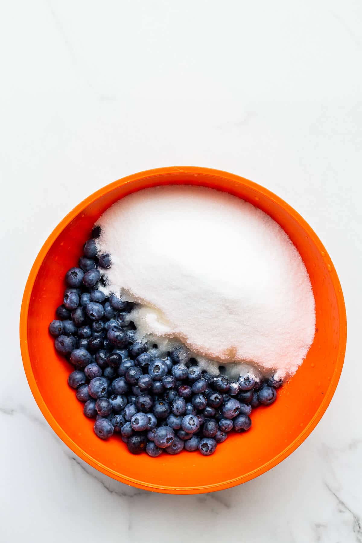 Macerating blueberries with sugar and lemon juice in a big bowl to make homemade blueberry jam.