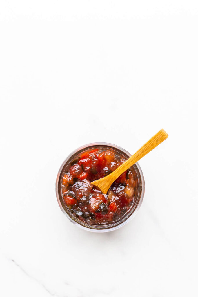 A jar of jalapeño jam with a small wooden spoon for serving.