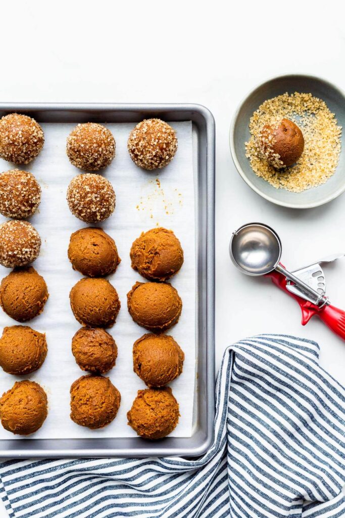 Rolling scoops of molasses cookie dough in turbinado sugar to coat them before baking.