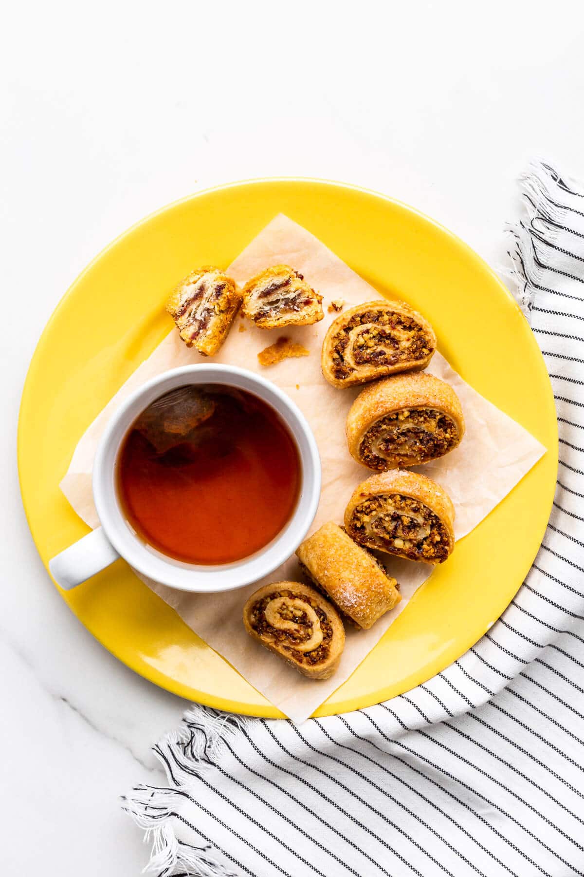 Rugelach cookies on a yellow plate with a cup of tea.