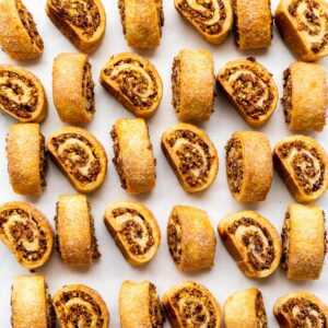 Rugelach cookies, freshly baked, lined up on parchment paper to show the beautiful swirls of cream cheese cookie dough and cinnamon walnut filling.